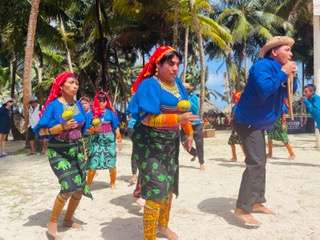 Four people in matching blue shirts performing a dance on the beach together